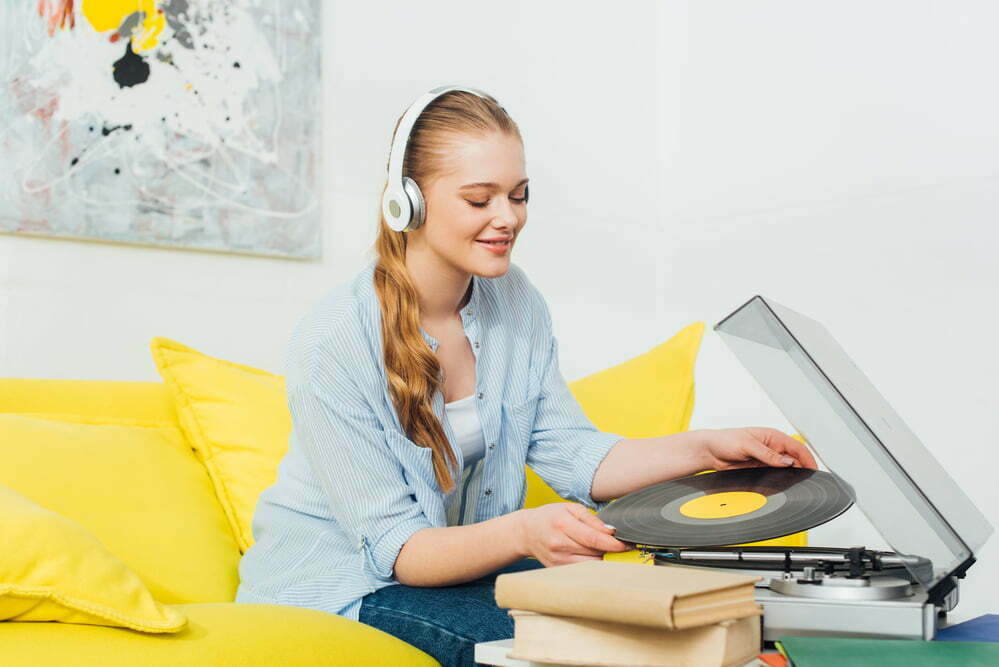 Smiling woman in headphones holding vinyl record near record player