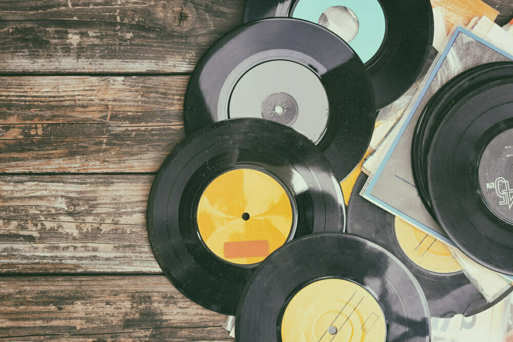 Multiple vinyl records stalked on a wooden floor.